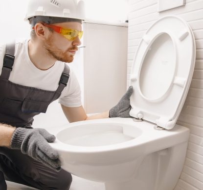 Plumber installing toilet bowl in restroom, work in bathroom.